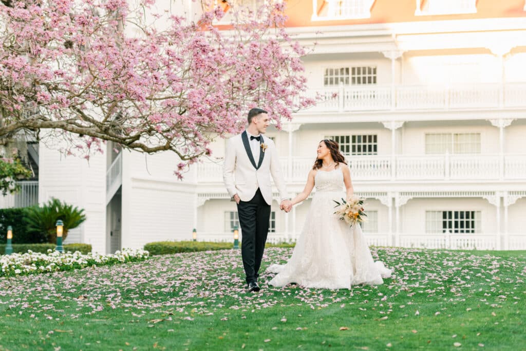 bride and groom walking across the lawn under a pink flowering tree by church