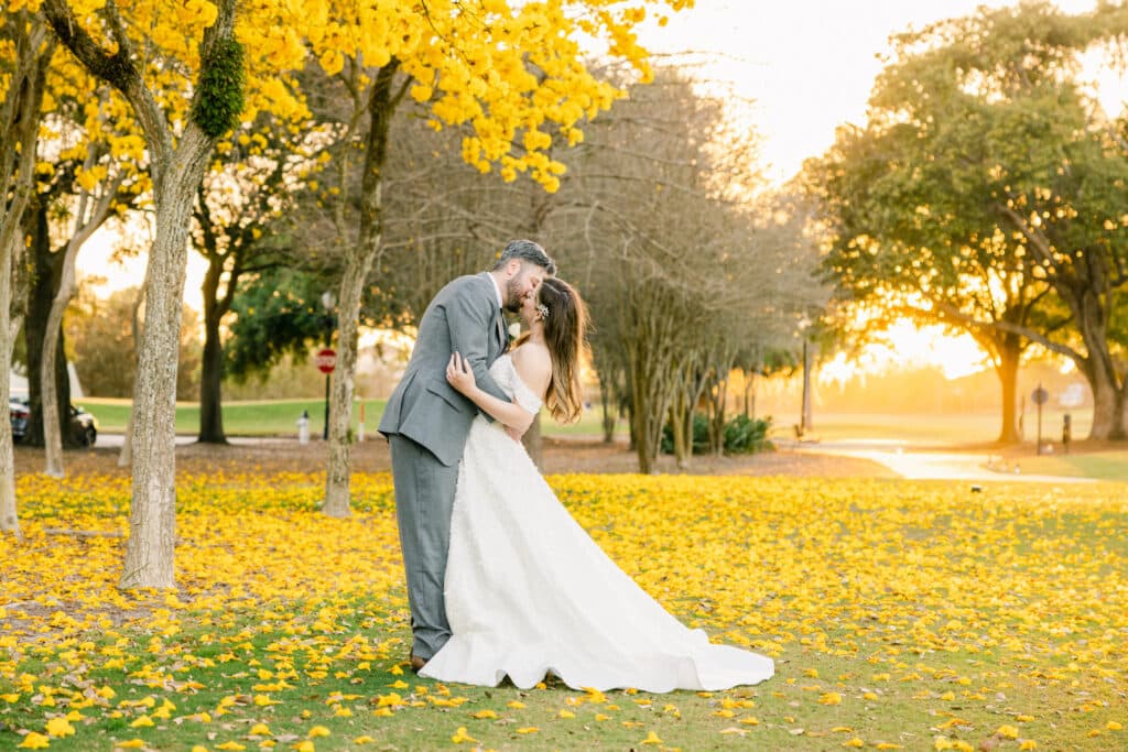 bride and groom kissing in a meadow of yellow leaves under a yellow flowering tree