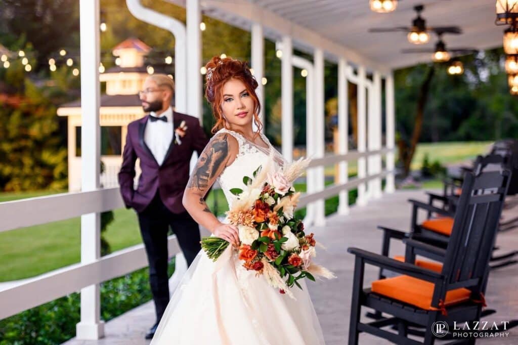 bride with a tattoo on her arm standing on a covered verandah with rocking chairs with orange cushions at The Carriage House at Vedder Farms
