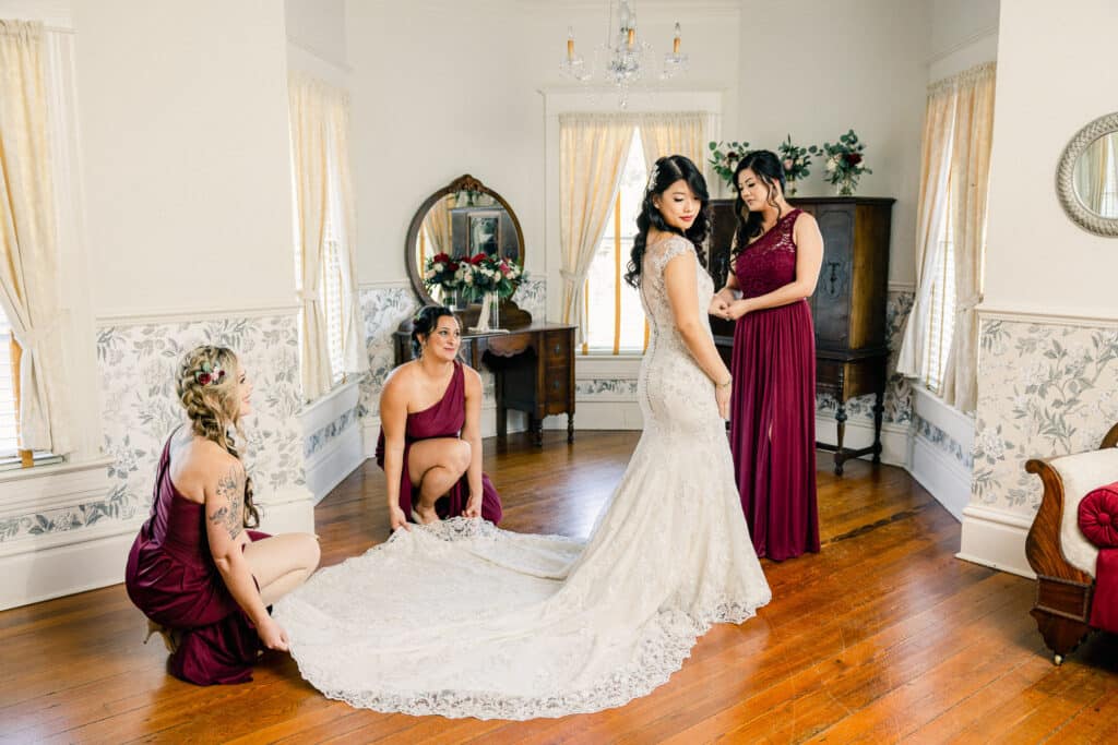 bride getting ready in an antique filled room with bridesmaids dressed in burgandy dresses