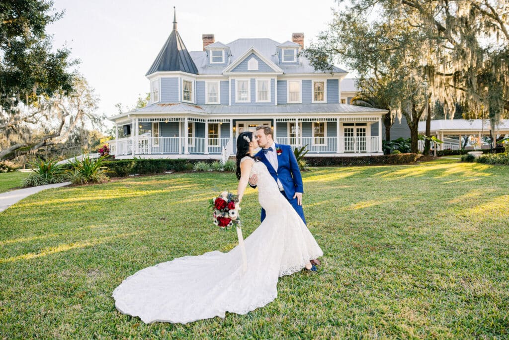 groom dipping his bride on the lawn in front of an old victorian home