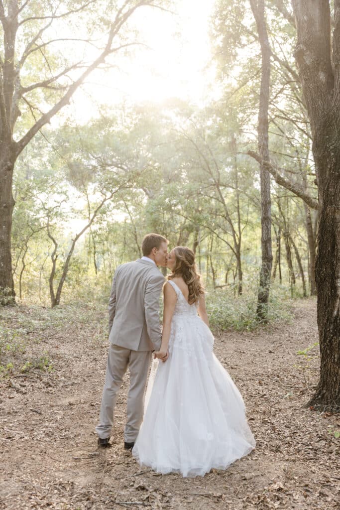 bride and groom walking in the woods with sun setting through the trees at The Carriage House at Vedder Farms