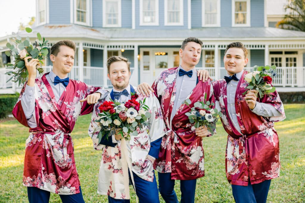 groom and groomsmen having fun posing in pink robes with flower bouquets, imitating bride and bridesmaids on wedding day