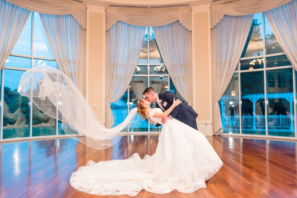 groom dipping his bride with her veil flowing against large windows photo by Jerzy Nieves Photography LLC