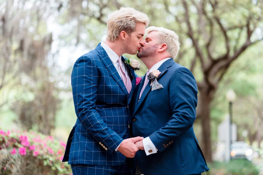 grooms in blue suits kissing and holding hands photo by Jerzy Nieves Photography LLC