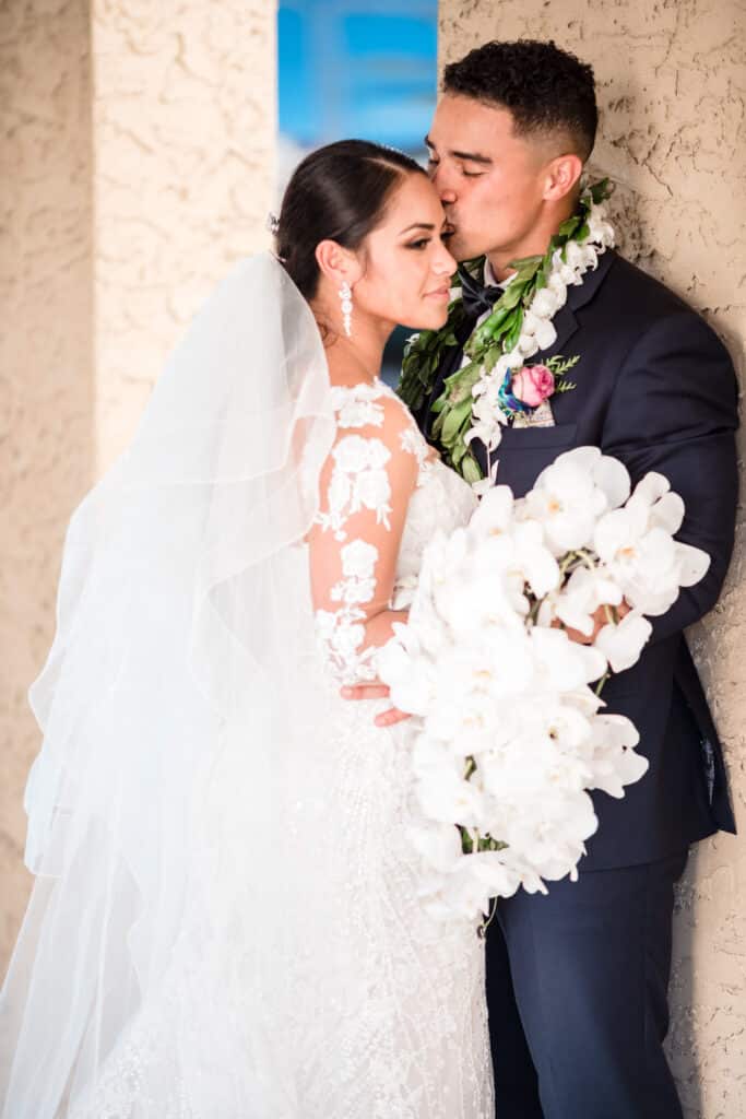 bride with stunning white bouquet and groom with lei kissing her temple photo by Jerzy Nieves Photography LLC