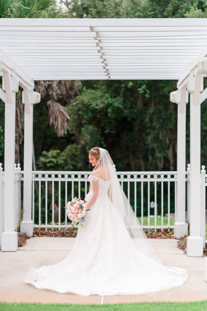 bride posing and showing the train of her wedding gown with veil and bouquet under wooden pergola photo by Jerzy Nieves Photography LLC