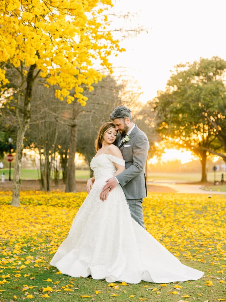 bride and groom sharing a moment under a yellow flowering tree and a lawn of yellow leaves