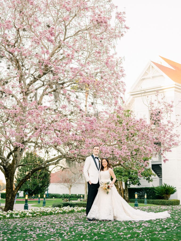 bride and groom on the lawn under flowering pink tree in front of the chapel