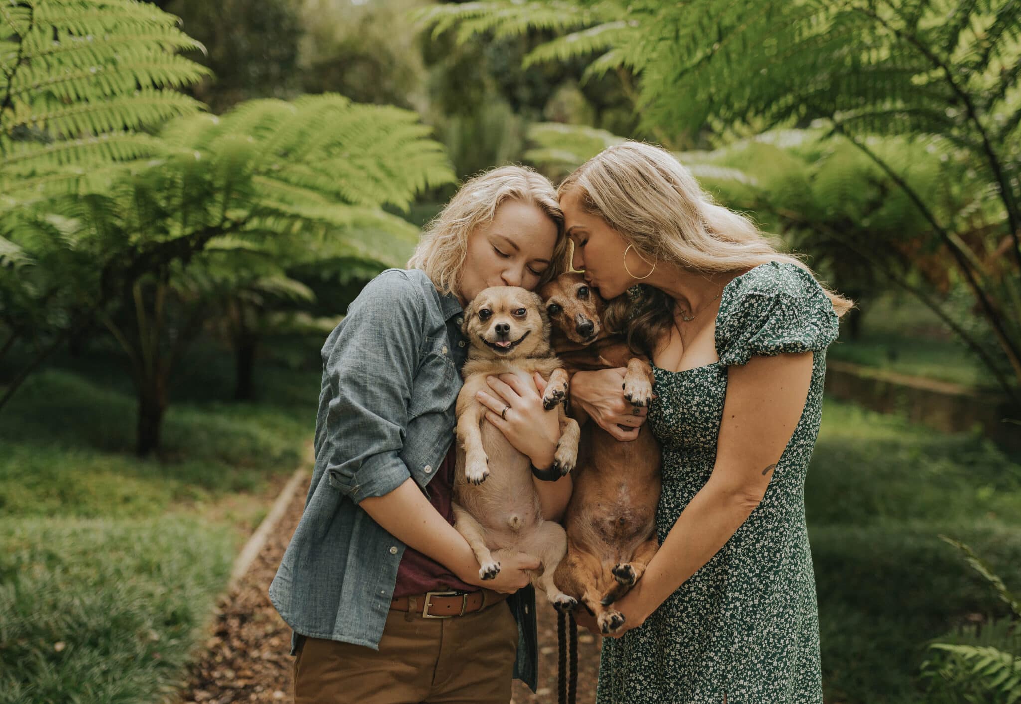 two woman holding small dogs up for picture kissing them