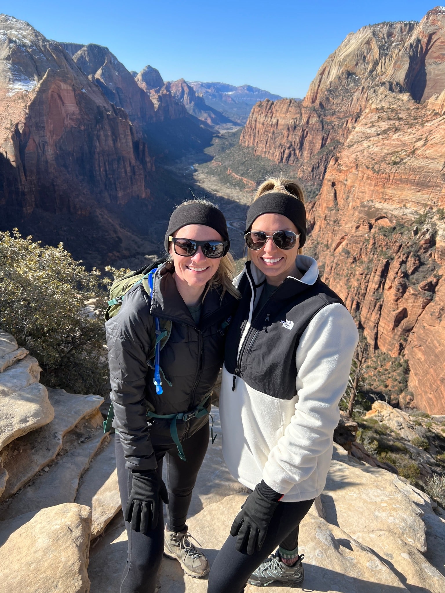 couple wearing jackets and gloves and sunglasses while hiking in a large canyon