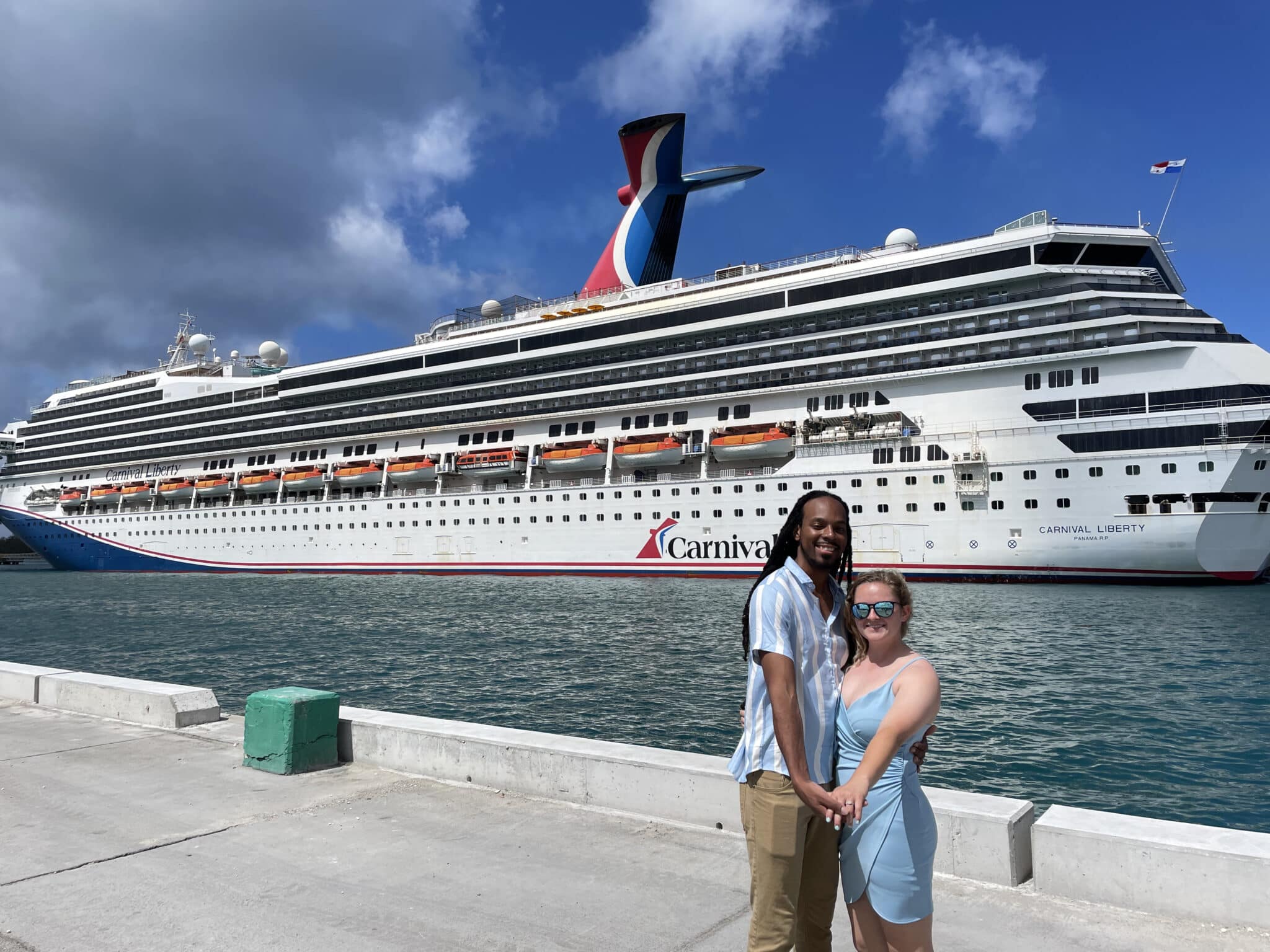 man and woman hold hands in front of them while standing together at a port in front of carnival cruise ship