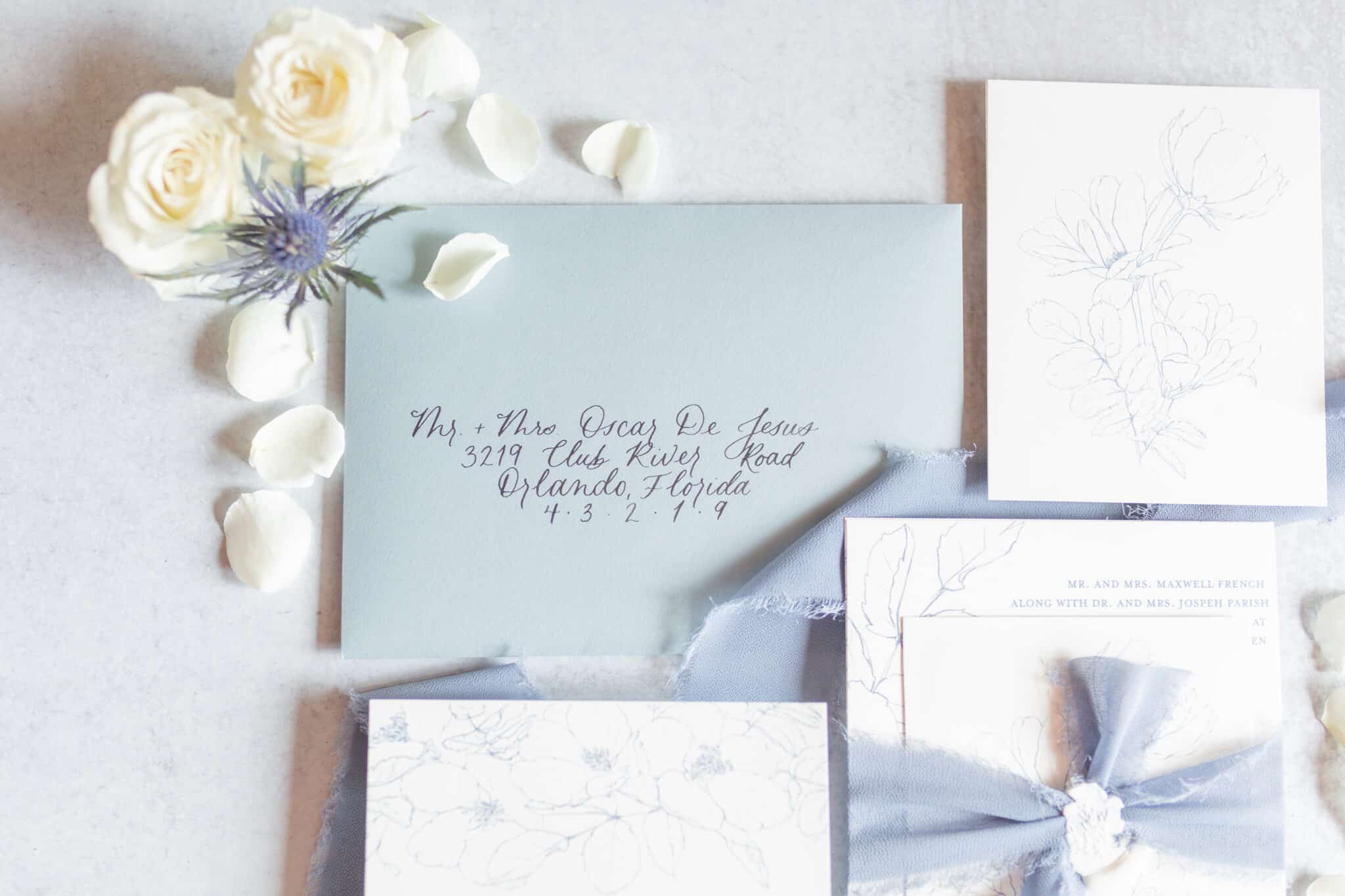 close up of invitation envelope with name written in cursive and flower petals scattered beside it
