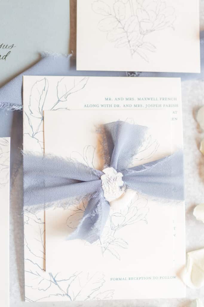 close up image of invitation suite tied together using dusty blue chiffon ribbon