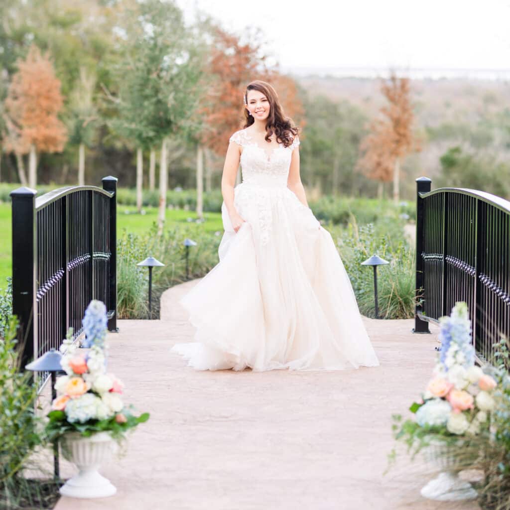bride moves around on bridge while wearing wedding dress smiling with trees in the background