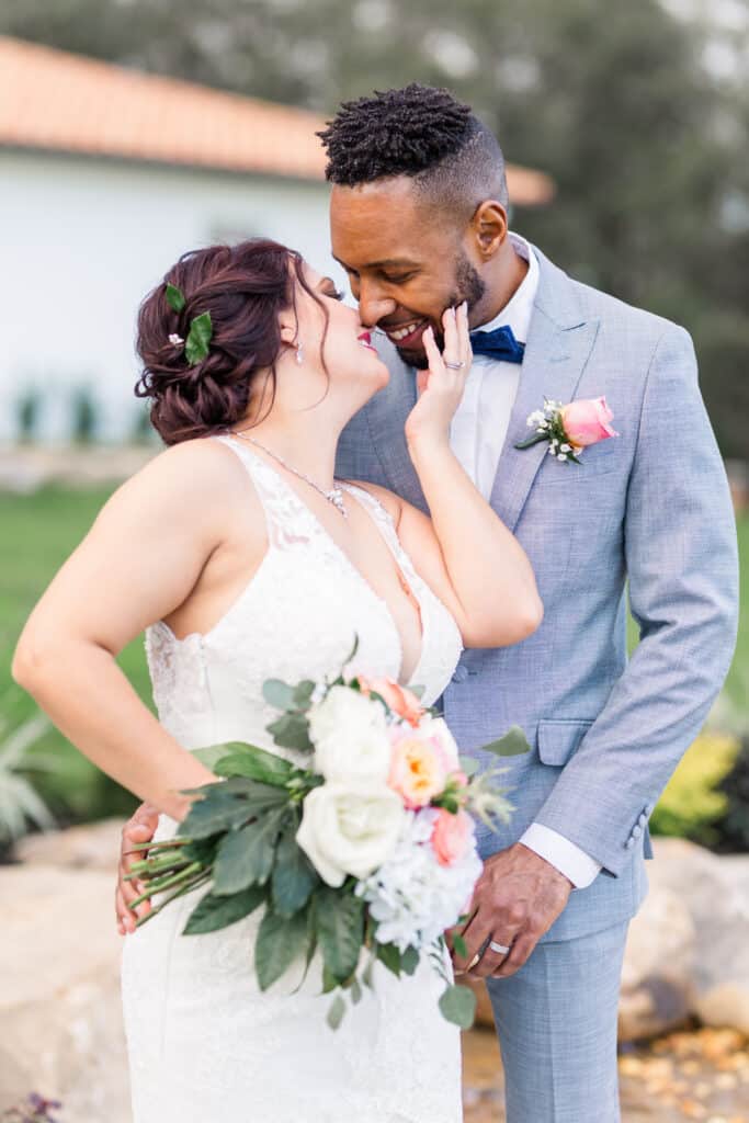 close up of man and woman on wedding day kissing while woman holds bouquet and man smiles