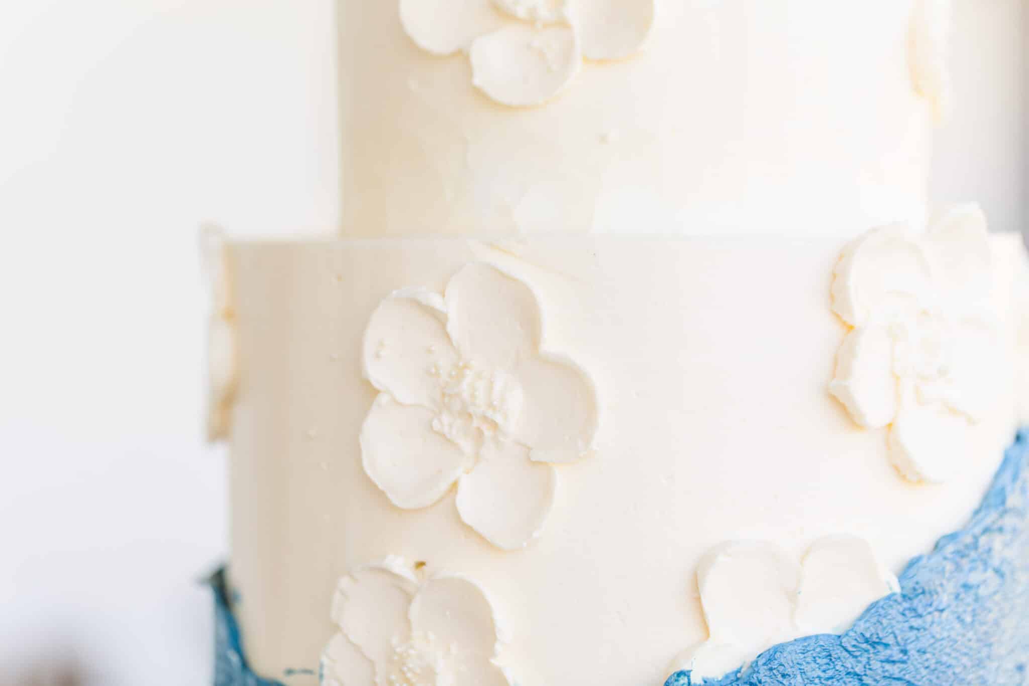 zoomed in image of cake with white fondant and decorated with white flowers made from frosting