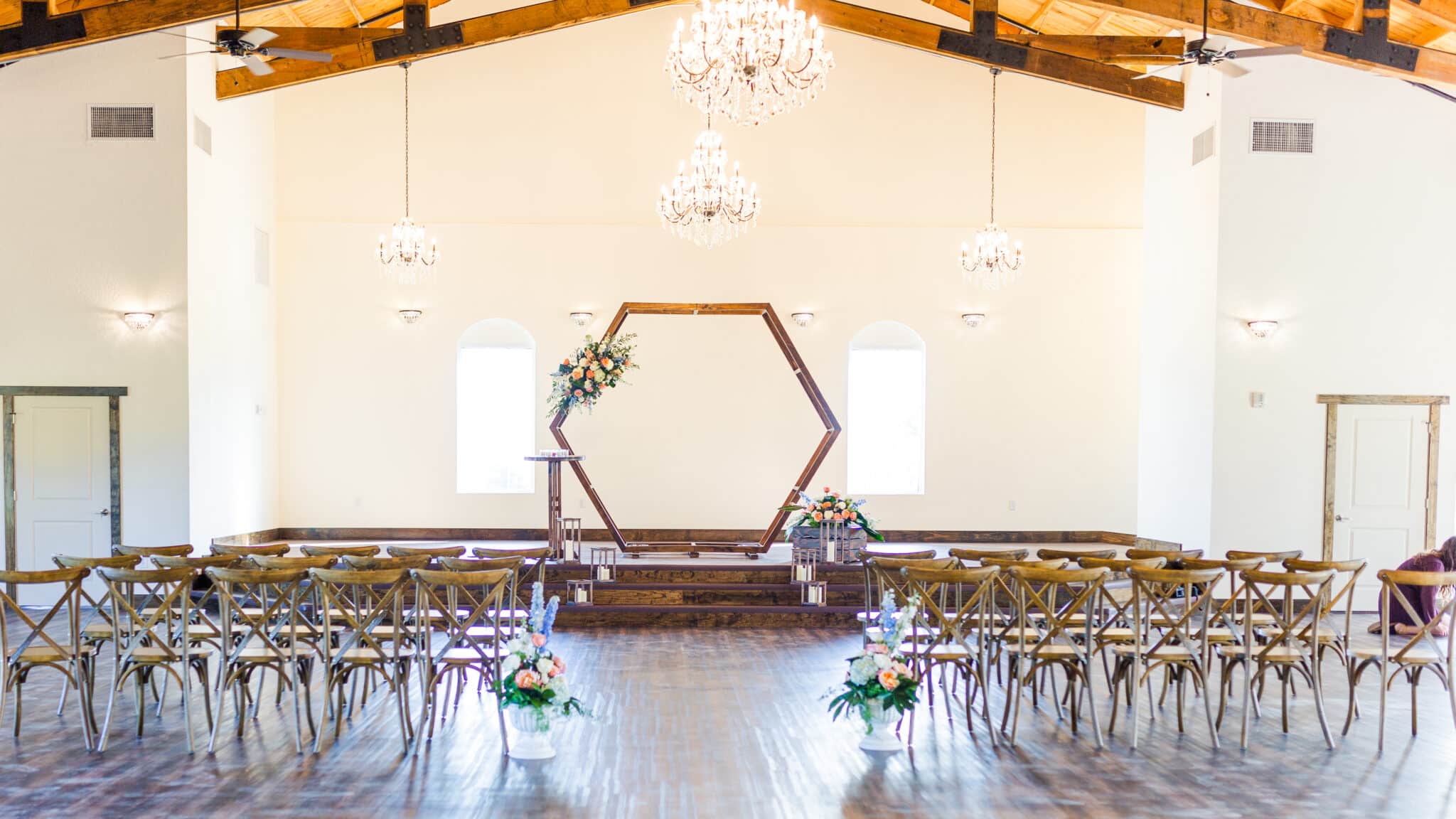 wedding ceremony with cross back chairs setup and wooden hexagon arch inside venue with wooden frame