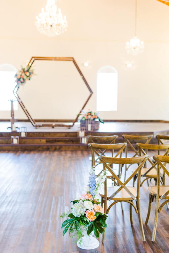 hexagon arch with floral decor on stage with chandelier above it