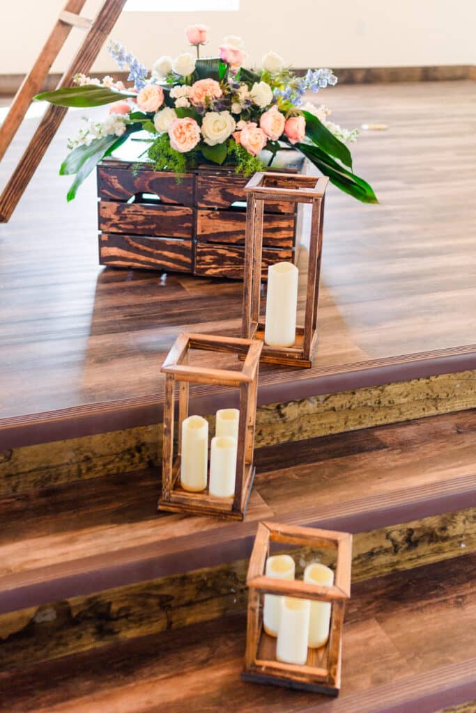 led candled in wooden structures sitting on wooden stairs with floral arrangement in background on wooden crates