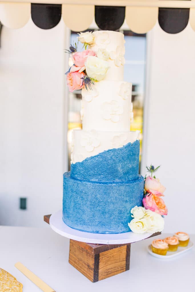 four tiered wedding cake with blue and white design on top of cake stand with white and pink floral decorating it