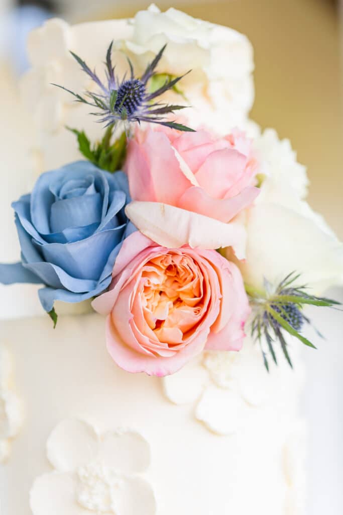 close up image of blue and pink roses decorating cake with white fondant flowers on it