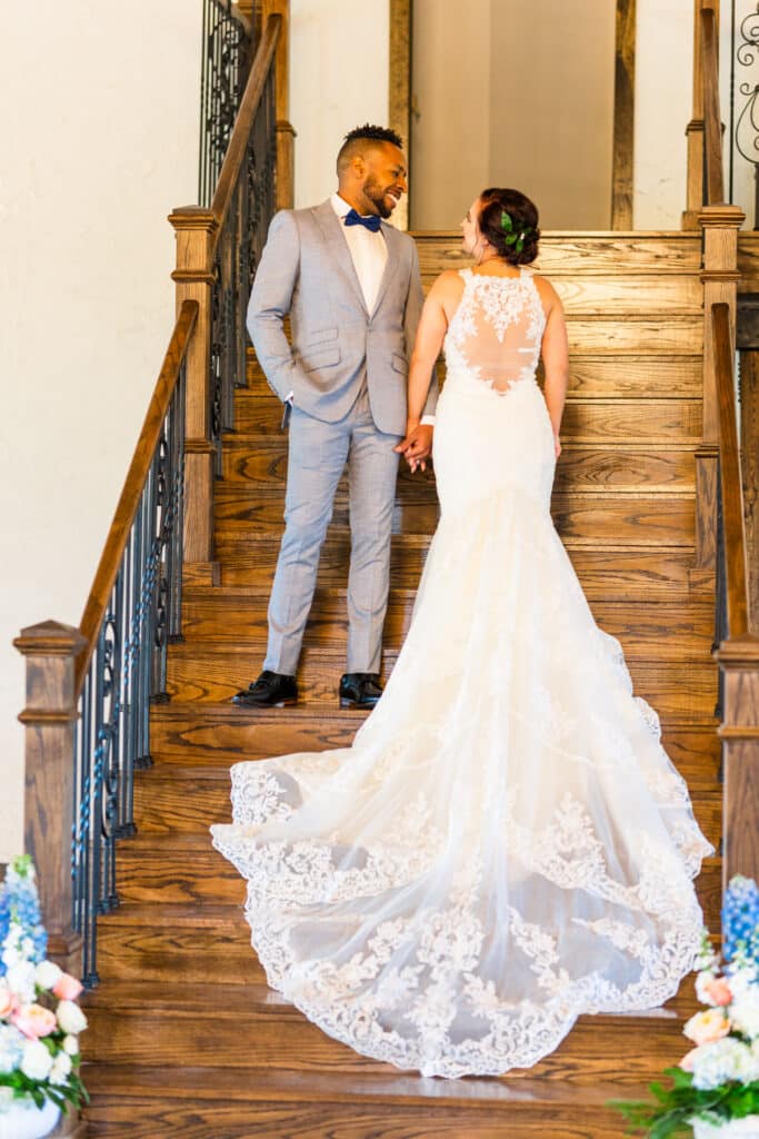 Bride and groom standing on wooden steps facing each other, holding hands, and smiling.