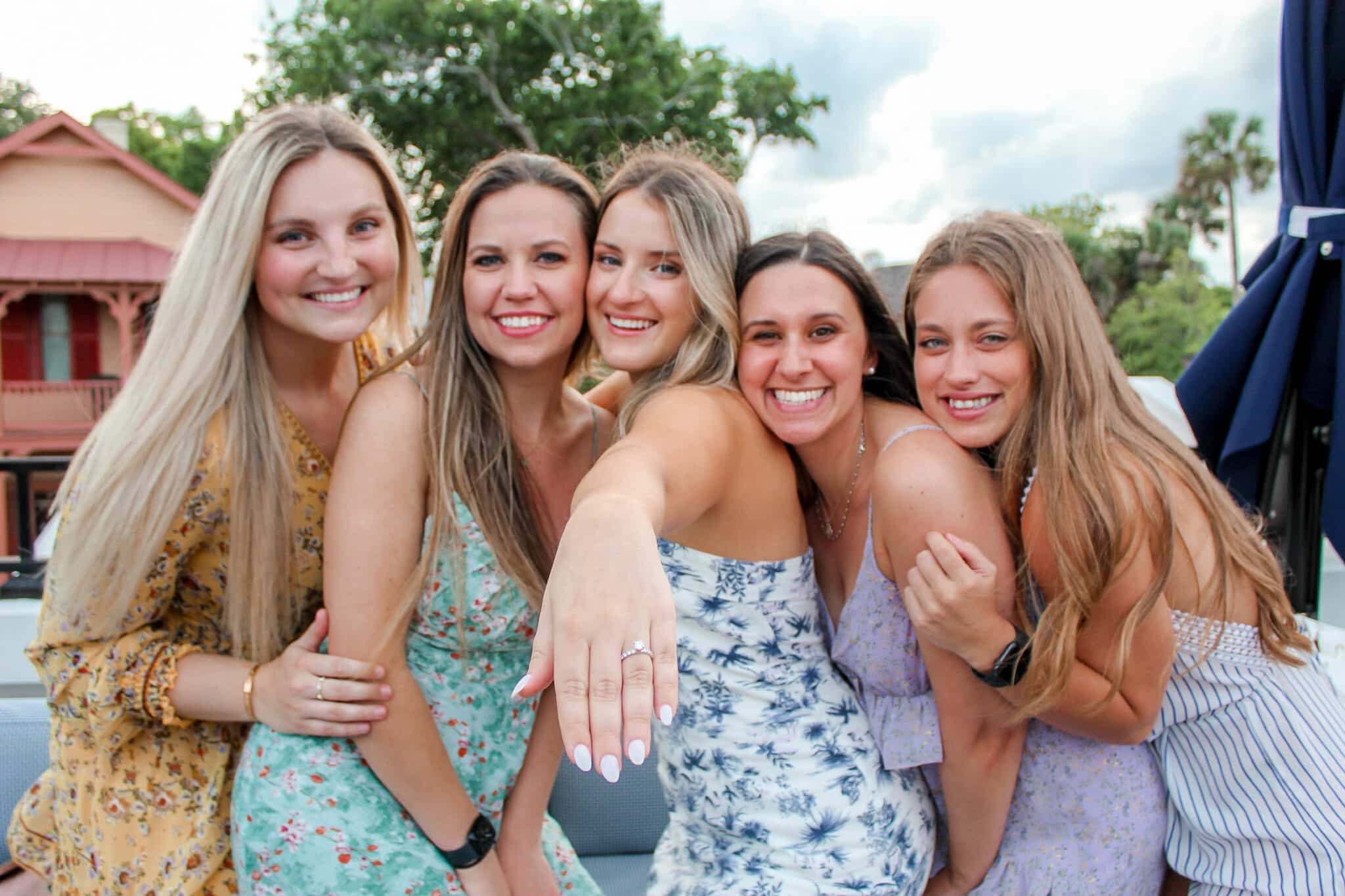 group of five girls stand together for picture smiling as girl in the middle holds out hand to show ring