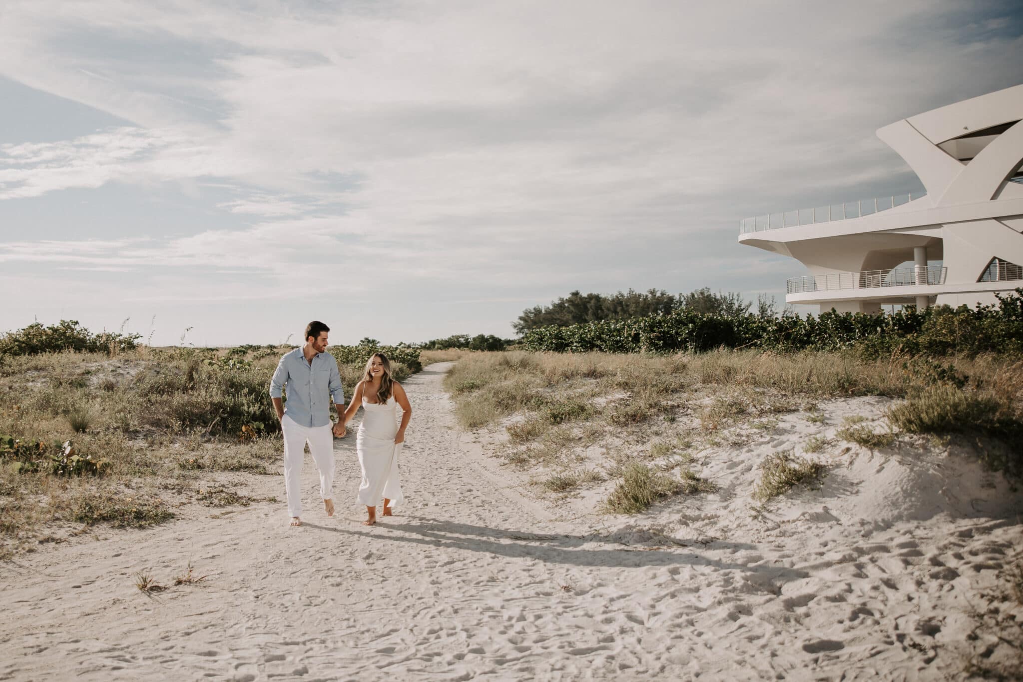 engaged couple walks togehter at the beach while taking engagement pictures