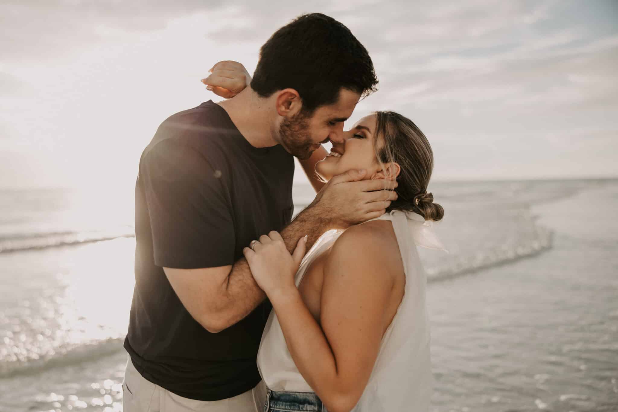 couple poses with noses touching about to kiss with ocean behind them