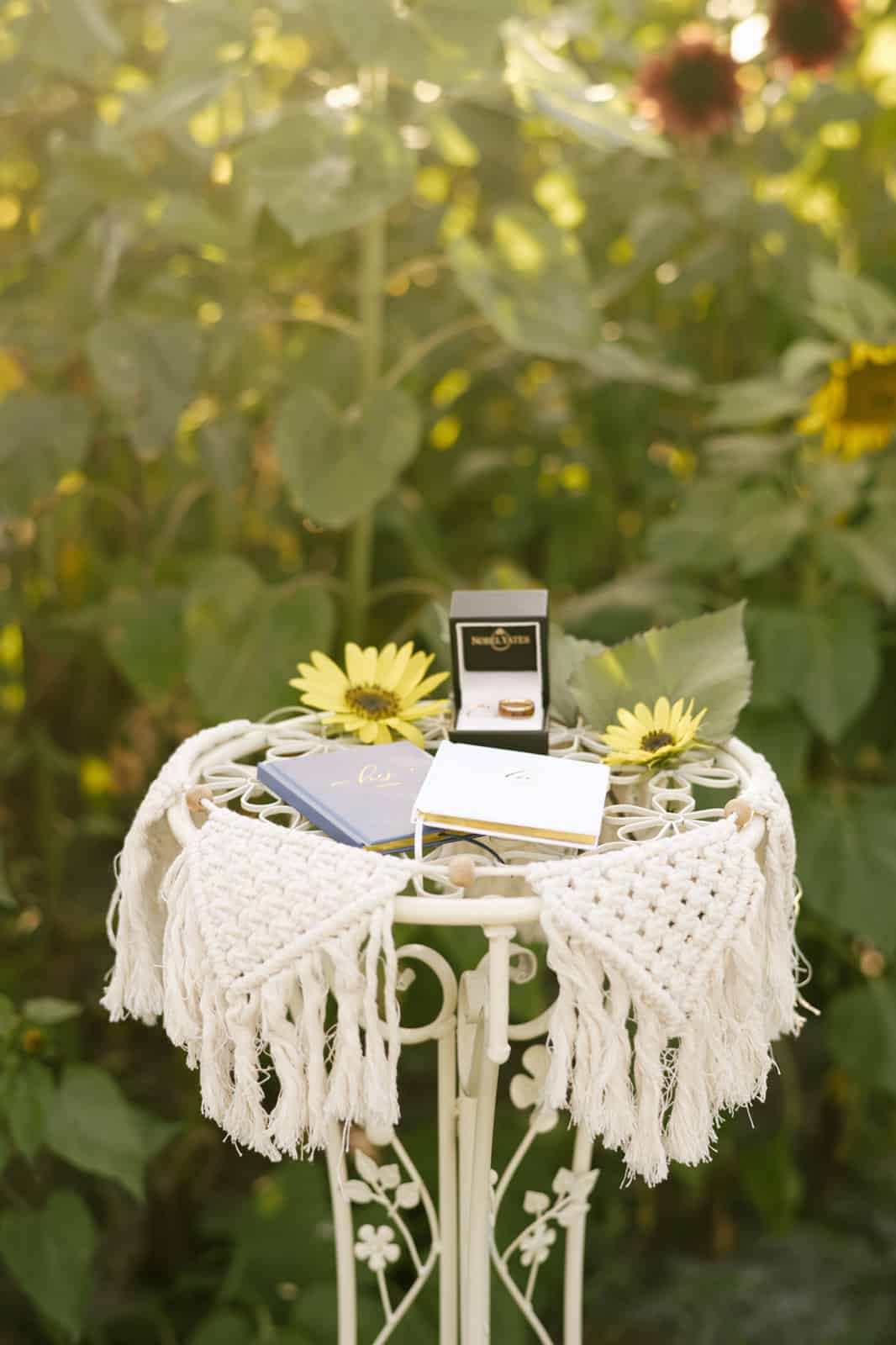 small table with macrame pieces hanging off the edges with vow books and ring box sitting on top for wedding ceremony