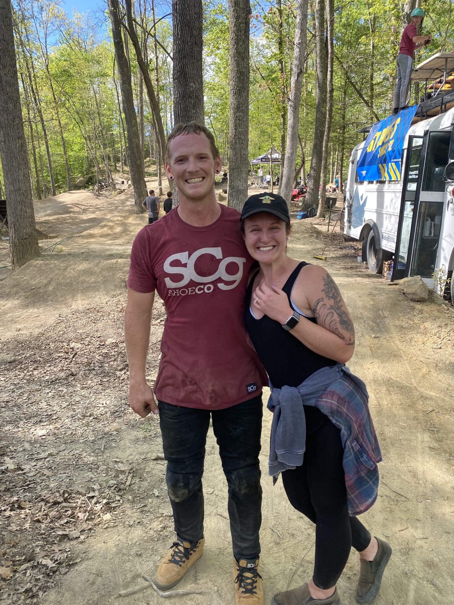 couple recently engaged stand together for picture in woods while smiling