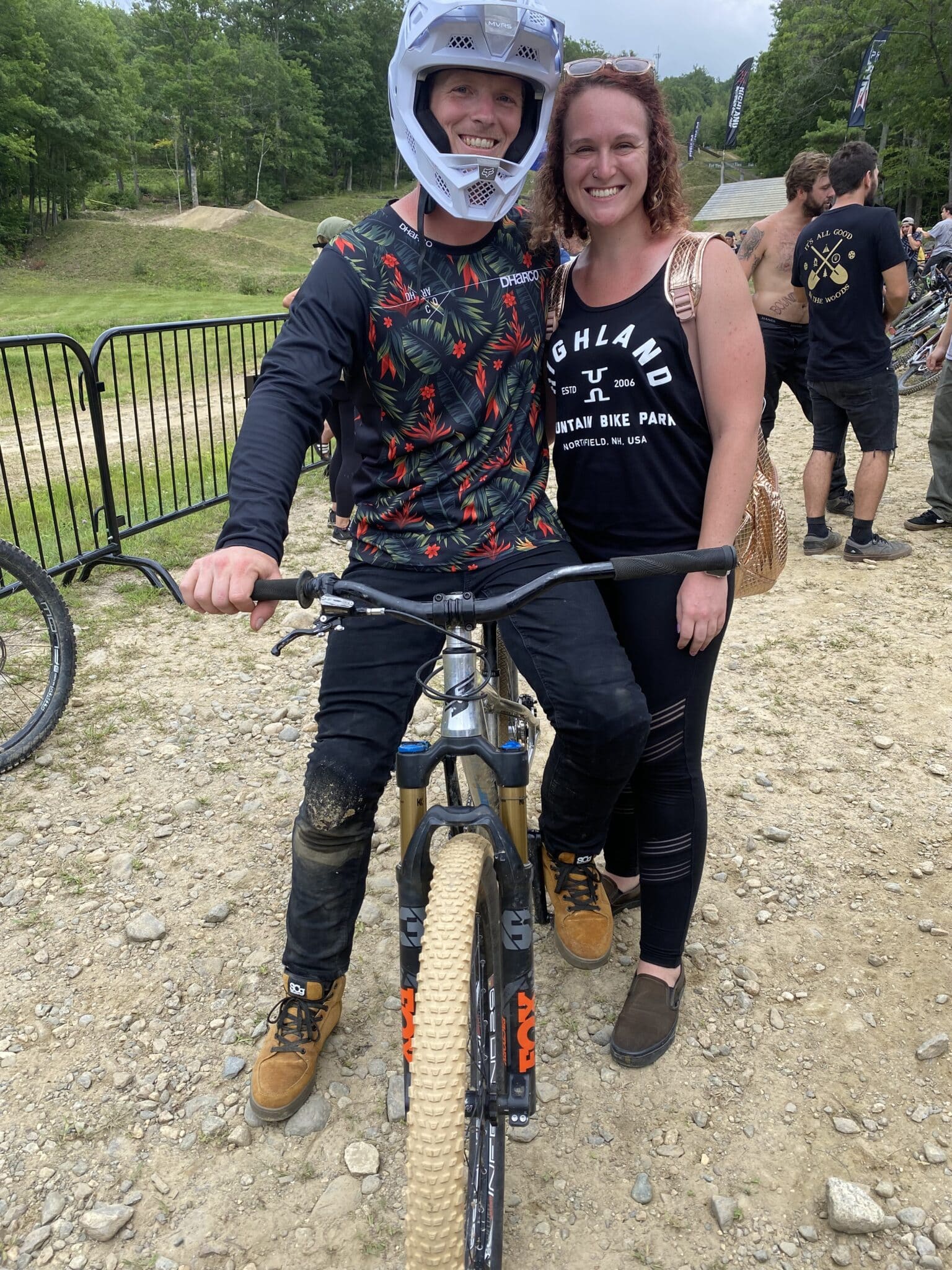 man sits on dirt bike wearing a helmet with arm around woman standing next to him
