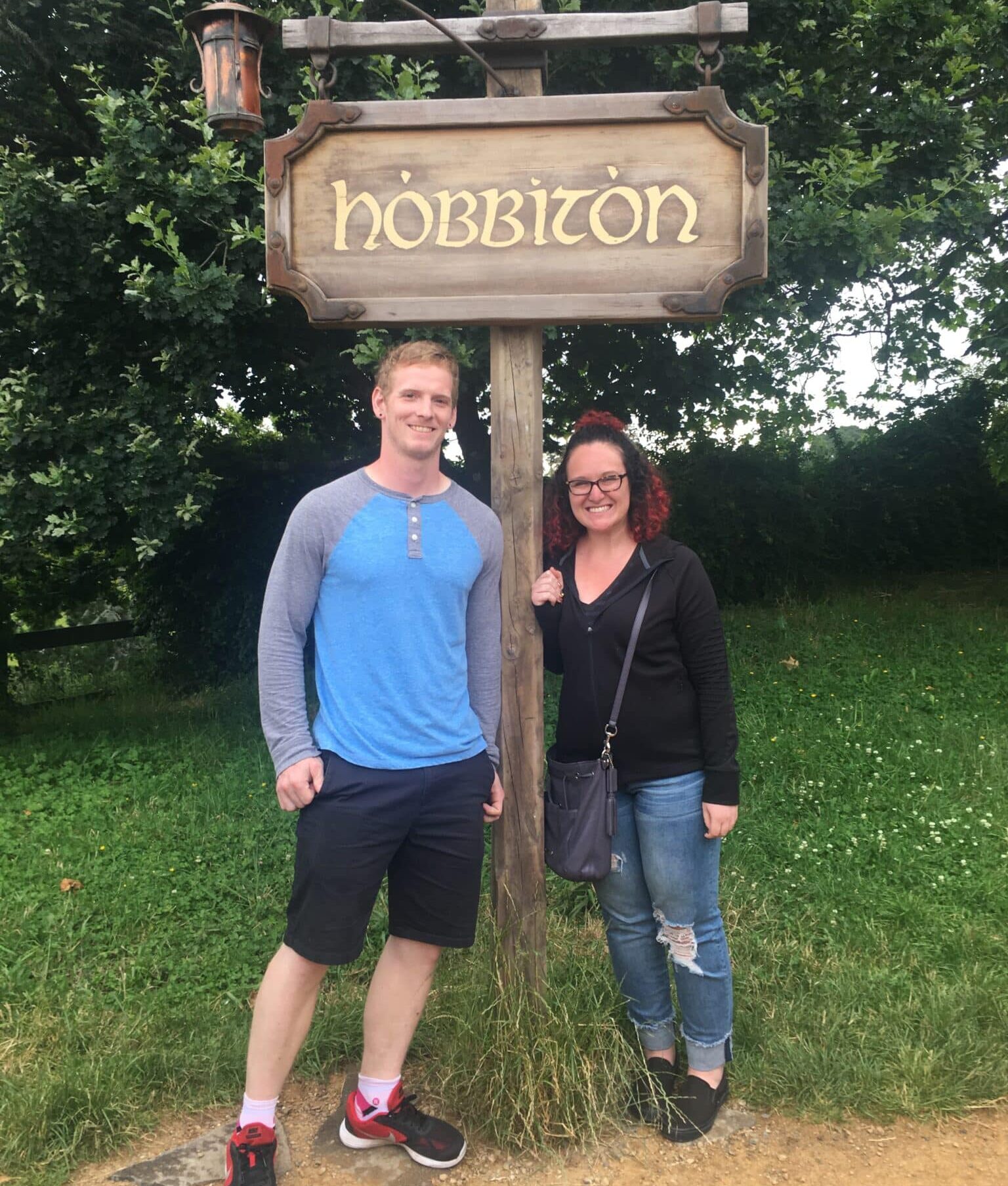 man and woman stand on opposite sides of sign that reads hobbiton
