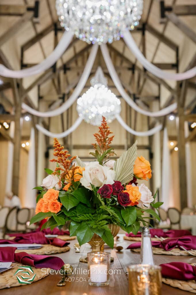 barn with white ceiling drape, crystal chandeliers and tablescapes in bright colors and gold accents at The Barn at Hidden Oaks Farm of Lake Mary