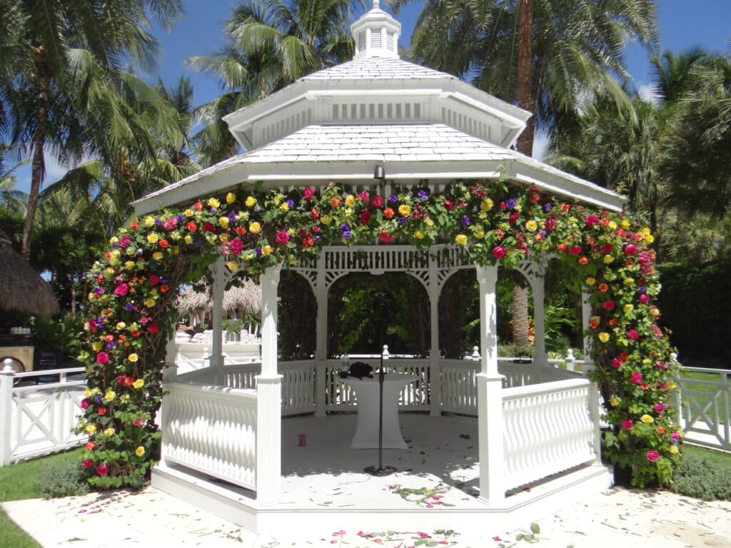white southern outdoor pergola draped with green swag with orange, yellow and red flowers
