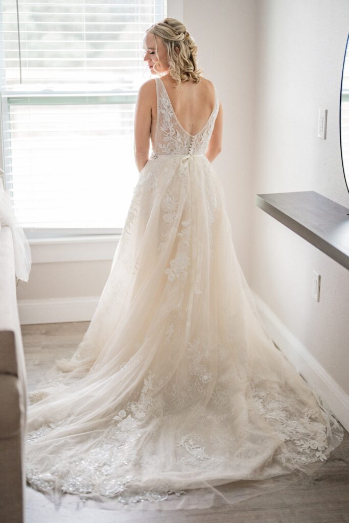 bride standing at window showing the back of her wedding dress and train