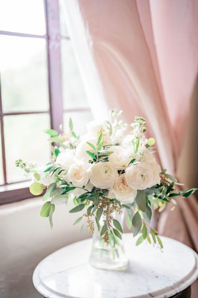 floral arrangement on a side table with a pink curtain and a window in the background