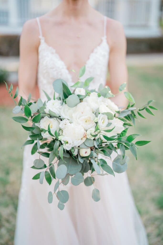 bride showing bridal bouquet with eucalyptus and white roses and peonies