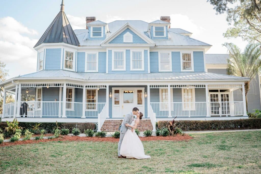 groom dipping bride to pose for photo on lawn in front of blue victorian home