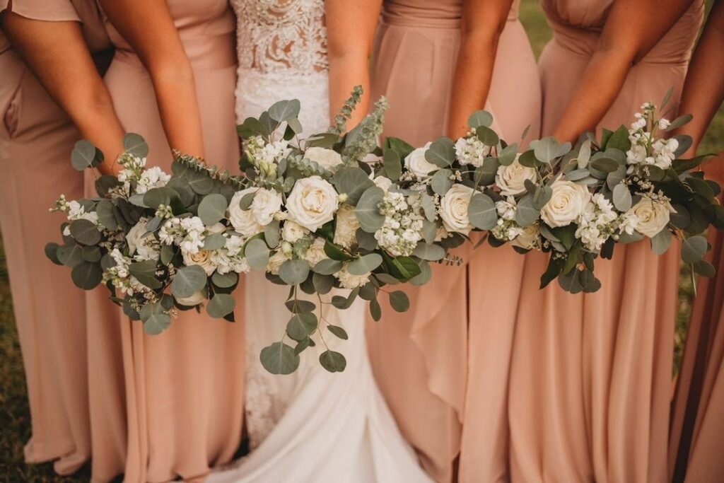 collection of bridal bouquets from Sweet Pea Design Collective against wedding gown and blush bridesmaids dresses