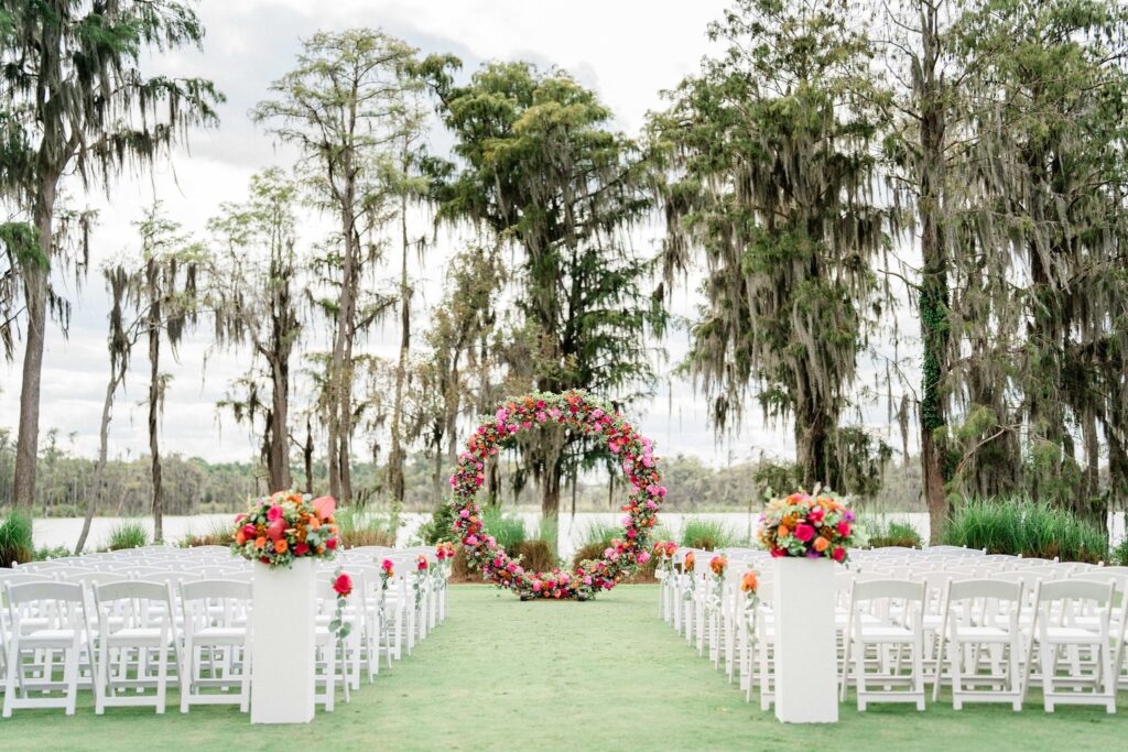 outdoor wedding reception with white chairs and large altar of ring of flowers and greenery