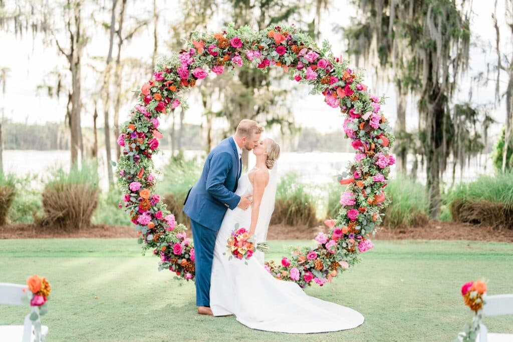 groom dipping bride in front of large ring flower altar in pinks, reds and white flowers
