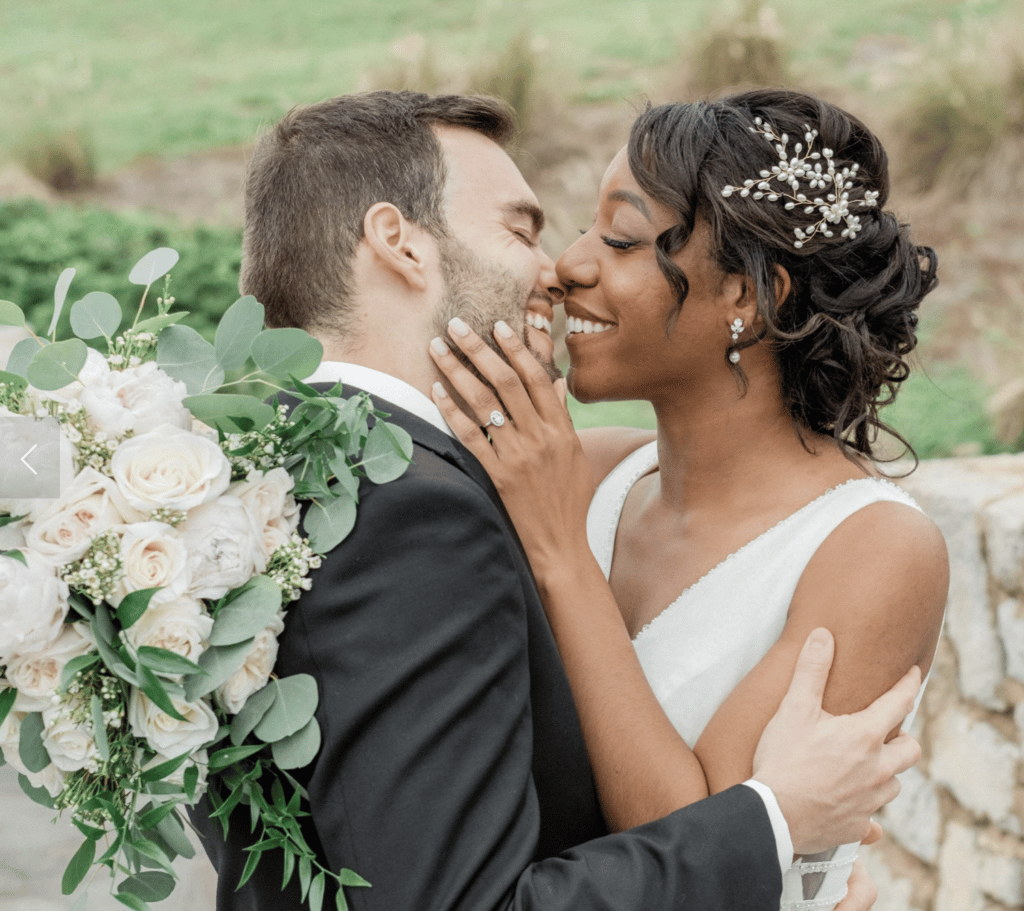 bride with sprigs of flowers in her hair and bouquet of white flowers and groom kissing