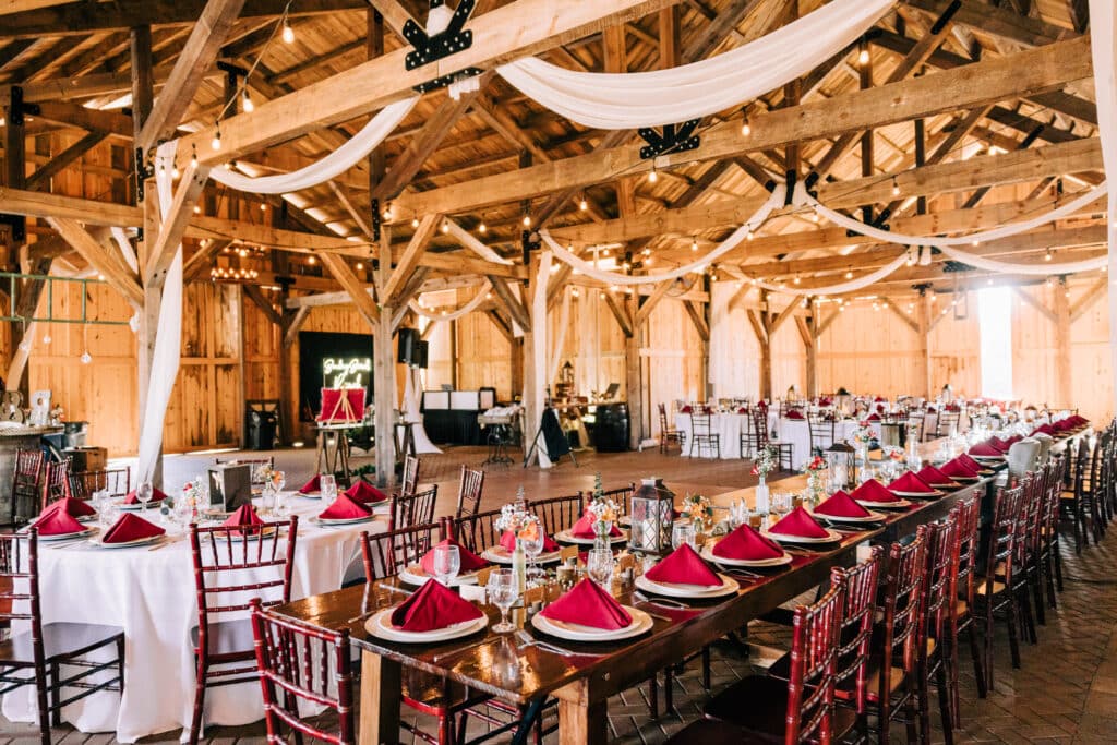 wedding reception area with wood tables and post and beam interior, set with red accents at Bending Branch Ranch in New Smyrna Beach, FL