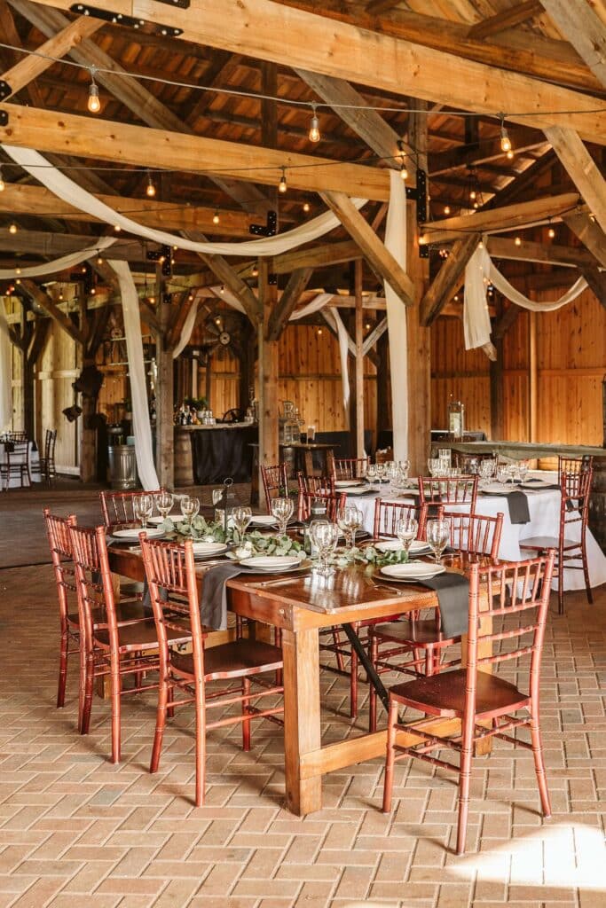 post and beam barn with wooden tables and chairs, white draping and green and white table accents at Bending Branch Ranch in New Smyrna Beach, FL