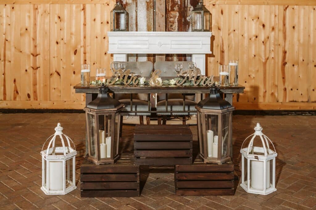 wooden sweetheart table with greenery and white lanterns against a fireplace mantel at Bending Branch Ranch in New Smyrna Beach, FL