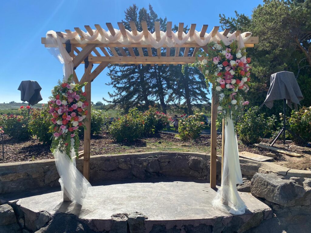 wooden pergola with rustic floral arrangement and fabric swags on a hill with a blue sky in the background
