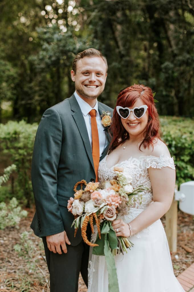bride with bouquet of roses in oranges and tan by Sweet Pea Design Collective and groom with an orange tie