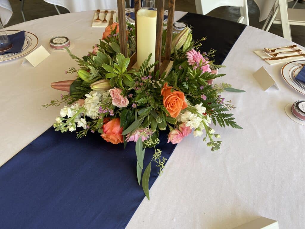 navy runner center piece with coral and cream flowers and cream candle in a hurricane lamp